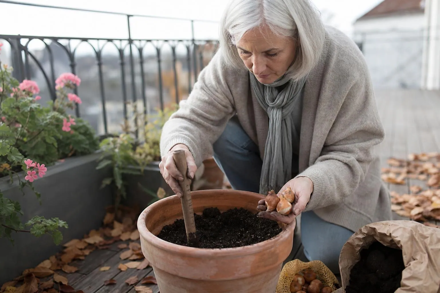 Femme d’une cinquantaine d’années plantant des bulbes au plantoir dans une jardinière de balcon, un matin clair d’automne